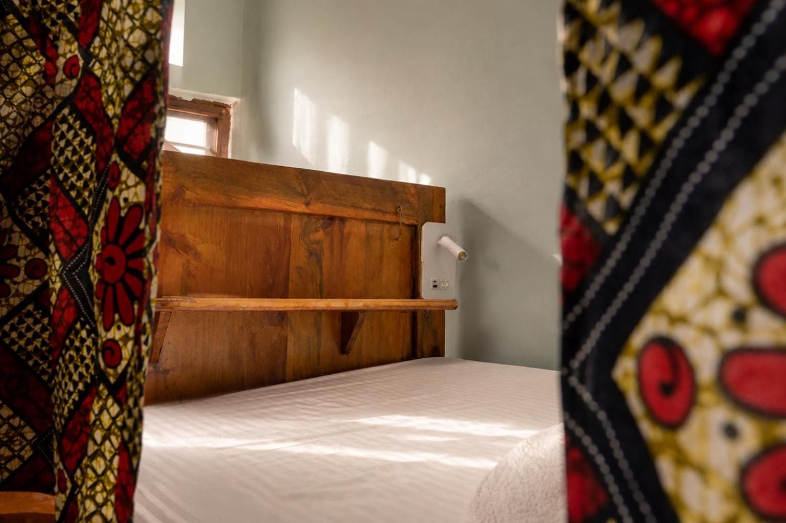 a bunk bed with a patterned kitenge curtain and white linen