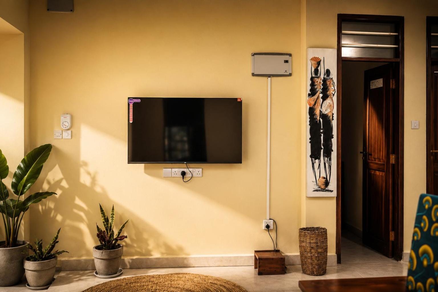 a flat-screen on a whitewashed wall beside a carved teak door