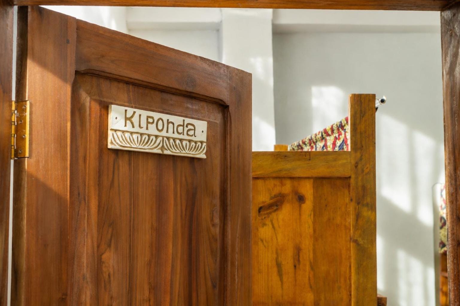 a carved plaque reading Kiponda on a teak door, opening onto a bunk room