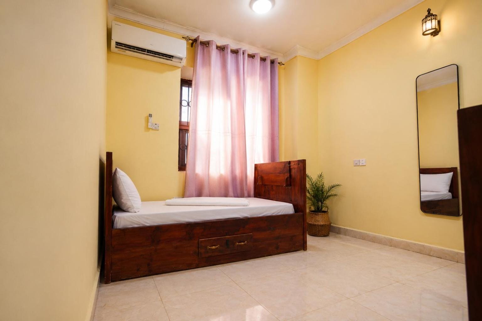 a solid teak double bed in a pale room with sheer curtains