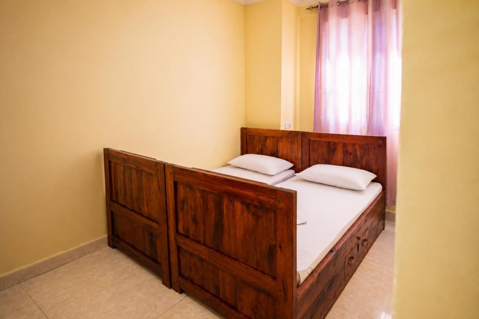 a made teak bed with two pillows under a window