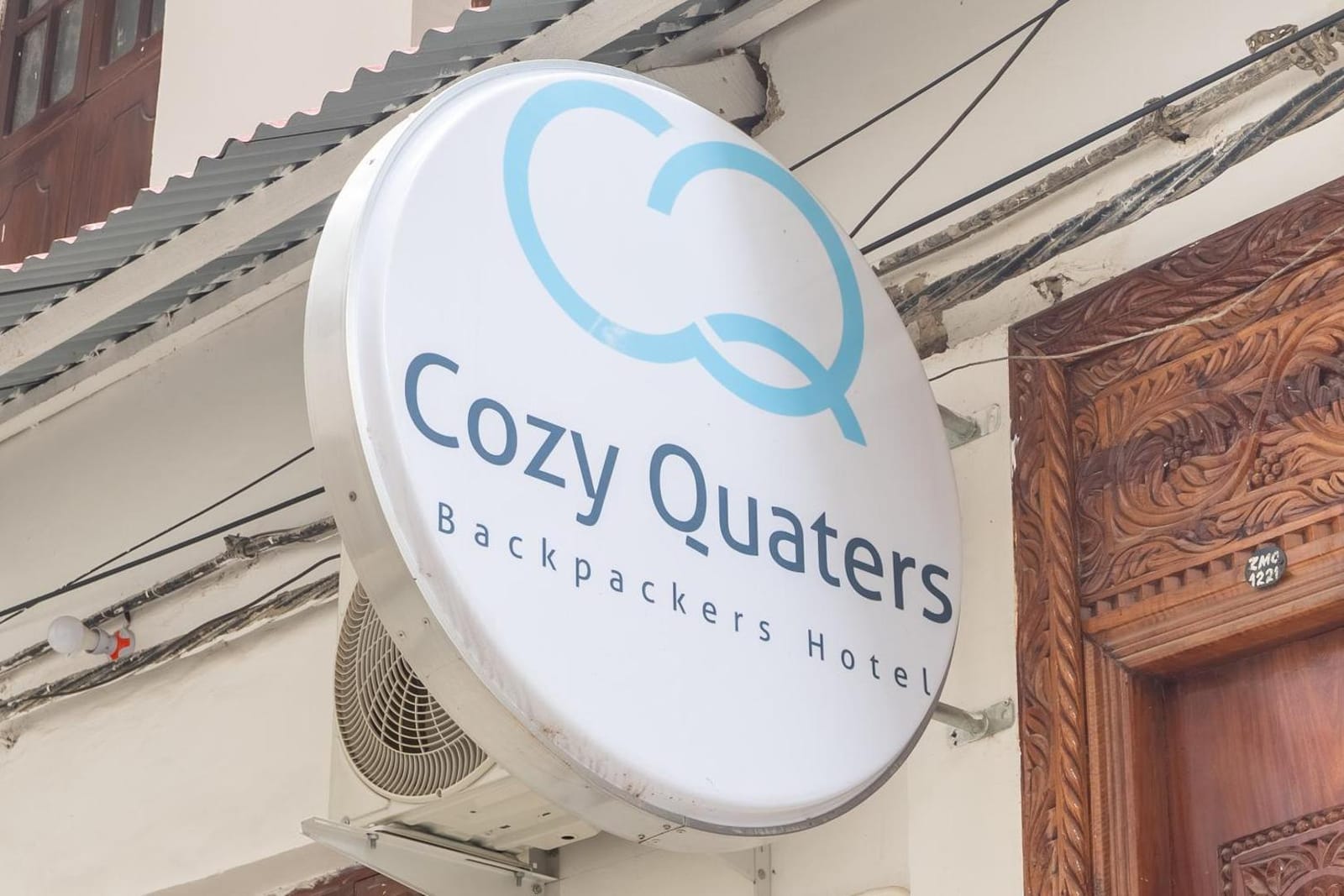 the round Cozy Quarters sign, a blue CQ monogram on white, beside a carved teak door